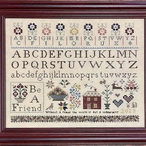 May include: A framed cross-stitch sampler with a colorful alphabet, flowers, and the phrase "Be A Friend". The sampler also includes the quote "Without a friend the world is but a wilderness" and the year 2023.