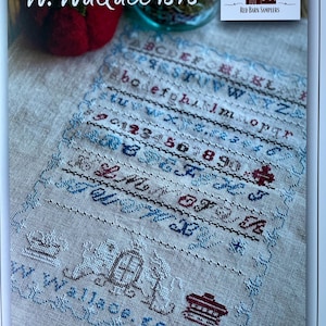 May include: A cross-stitch sampler with the text "W. Wallace 1878" in the upper left corner. The sampler features embroidered letters, numbers, and decorative elements in blue, red, and brown on a beige fabric. The Red Barn Samplers logo is in the upper right.