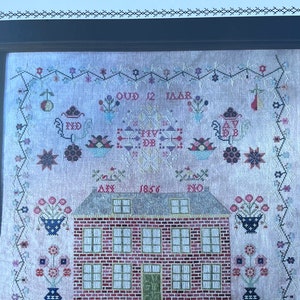 May include: A cross-stitch sampler featuring a brick house with a red roof and six windows. The house is surrounded by floral motifs and the text "My Father's House, Magdalena van der Býl 1856, OUD 12 JAAR, AX 1856, NO".