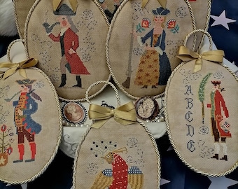 Puede incluir: Siete adornos ovalados de punto de aguja hechos a mano con un tema patriótico. Cada adorno presenta un diseño diferente, incluyendo un soldado colonial, un pájaro y una bandera. Los adornos están decorados con ribetes y cintas doradas.