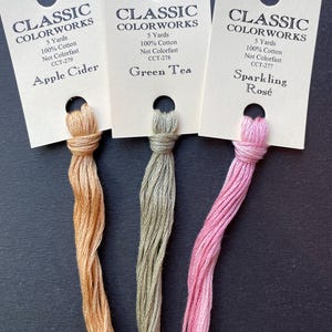 May include: Three skeins of embroidery floss in shades of orange, green, and pink. Each skein is labeled with the brand name "Classic Colorworks" and the color name: "Apple Cider", "Green Tea", and "Sparkling Rosé".