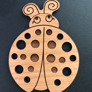 Peut inclure: Coccinelle en bois avec une teinte brune, présentant un design détaillé avec de grands yeux et un corps recouvert de petits cercles.