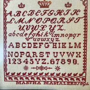 May include: A white cross-stitch sampler with red embroidery featuring the alphabet in uppercase and lowercase, numbers, and the text "MARTHA MASIALER57894".