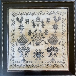 Może przedstawiać: Czarno-biały haftowany sampler z motywem kwiatowym, dwoma koszami kwiat&oacute;w, kogutkiem, jeleniem i dwiema postaciami trzymającymi laski. Sampler jest oprawiony w czarną ramę z ozdobnym obramowaniem z koralik&oacute;w. Na dole haftowany jest tekst "ELISABET. 18. 22. DOORIBOS".