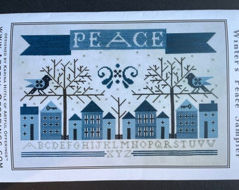 May include: A cross-stitch pattern for a sampler titled "Winter's Peace Sampler". The pattern features a winter scene with houses, trees, birds, and the word "PEACE" in a banner. The alphabet is also included in the pattern.