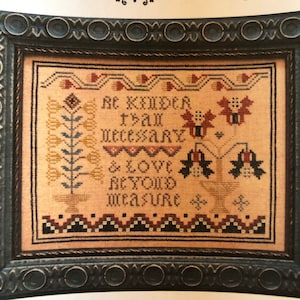 May include: Cross-stitch embroidery framed in a dark blue wood frame. The embroidery features a floral design with the text "Be kinder than necessary & love beyond measure".