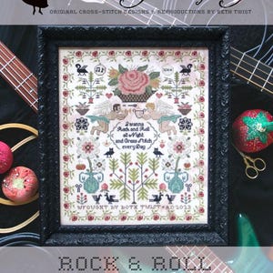 May include: A cross-stitch sampler with a white background and colorful floral and bird motifs. The text "I wanna Rock and Roll all Night and Grass Stitch every Day" is stitched in black thread. The sampler is framed in a black frame and is titled "Rock & Roll Sampler".