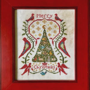 May include: A cross-stitch embroidery in a red wooden frame featuring a central green Christmas tree decorated with small figures, surrounded by red birds and green vines, with the text Merry Christmas stitched in red thread.
