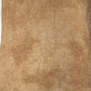 May include: Close-up of a tan burlap fabric with a woven texture. The fabric has a natural, earthy tone and a slightly rough appearance. The weave is visible, creating a grid-like pattern across the surface. This material is suitable for various craft and home decor projects.