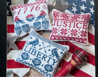 May include: Three small white pillow covers with red and blue embroidery. The pillows feature the words "1776", "Justice", and "Liberty" with a bird design. The pillows are displayed on a red, white, and blue striped fabric background. The title "Little Liberties" is displayed at the bottom of the image.