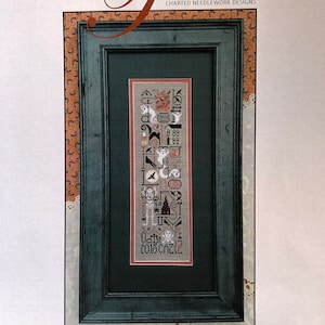 May include: A framed cross-stitch sampler titled "The Haunting" by The Drawn Thread. The sampler features Halloween-themed motifs in black, white, and orange, including ghosts, bats, and a haunted house. The frame is dark green.