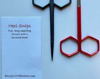 Op de afbeelding: Twee scharen met zeshoekige handvatten. Een paar is zwart met een puntige punt en het andere is rood met een afgeronde punt. De tekst op de kaart luidt "Hexi Snips Fun, long reaching Scissors with a Serrated blade KELMSCOTTDESIGNS.com".