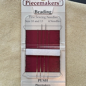 May include: A package of Piecemakers beading needles. The package is clear plastic with a burgundy-colored backing. The text on the package reads "Beading", "Fine Sewing Needles", "Size 10 and 13", and "4 Needles". The package also includes the text "PUSH".