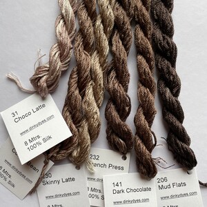 May include: Five spools of 100% silk embroidery floss in shades of brown, from light beige to dark brown. The spools are labeled with the color name, the length of the floss, and the website "www.dinkydyes.com".