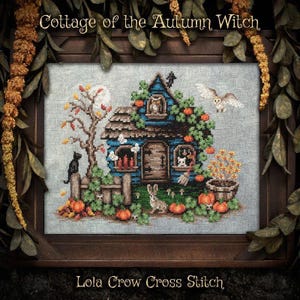 May include: A cross stitch pattern titled Cottage of the Autumn Witch by Lola Crow Cross Stitch. The design features a blue house with a brown roof, a black cat, a white owl, a rabbit, pumpkins, and autumn foliage on a gray fabric background.