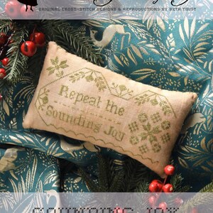 May include: A rectangular, beige cross-stitch pillow with the text "Repeat the Sounding Joy" in green thread. The pillow is surrounded by greenery and red berries, with the words "Heartstring Samplery" at the top.