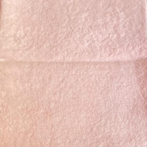 May include: A close-up of a pale pink fabric with a subtle textured pattern. The fabric has a slightly wrinkled appearance.