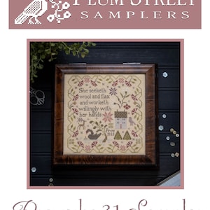 May include: A framed cross-stitch sampler with a brown wooden frame. The sampler features a beige background with colorful floral embroidery and the text "She seeketh wool and flax and worketh willingly with her hands: Prov 3113" in brown thread. The sampler is titled "Proverbs 31 Sampler" with the text "Original Designs by Paulette Stewart" below.