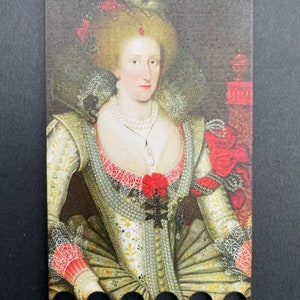 Peut inclure: Un portrait d'une femme vêtue d'une robe blanche et dorée avec des accents rouges. Elle porte un collier de perles et a une fleur rouge dans les cheveux. Le portrait est encadré dans un cadre en bois avec des trous autour du bord.