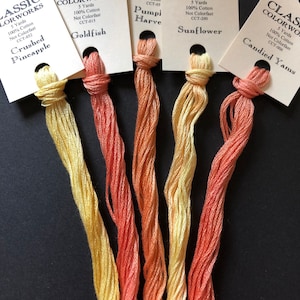 May include: Five skeins of embroidery floss in shades of yellow, orange, and red. The floss is labeled with the brand name "Classic Colorworks" and the color names "Crushed Pineapple", "Goldfish", "Pumpkin Harvest", "Sunflower", and "Candied Yams".