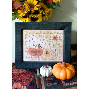 May include: A framed cross-stitch design featuring a pumpkin with the text "October 31" and a bee. The design also includes the alphabet and the word "BOO" with pumpkins and sunflowers.