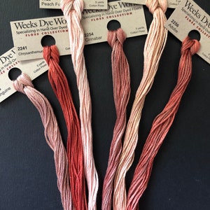 May include: Five spools of Weeks Dye Works floss in shades of peach, coral, and red. Each spool is labeled with the brand name, "Weeks Dye Works", "Floss Collection", and a color name and number. The colors are: 1129 Peach Fuzz, 2241 Chrysanthemum, 2254 Cinnabar, 1131 Peach, and 2256 Adobe.