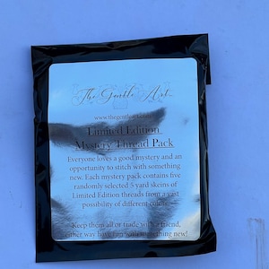 May include: A black package with a silver label featuring the text "The Gentle Art" and "Limited Edition Mystery Thread Pack." The label describes the contents as five randomly selected 5-yard skeins of thread.