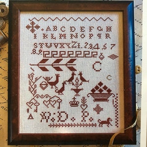 May include: A framed cross-stitch sampler with a brown wooden frame. The sampler features a red alphabet, numbers, and a design with birds, a crown, and a basket of fruit. The text on the sampler reads "Red Sampler".