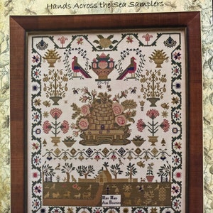 May include: A framed cross-stitch sampler with a floral design and a small house in the bottom. The sampler is titled "Miss Mary Ann Bournes 1791" and includes the text "Hands Across the Sea Samplers".
