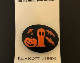 May include: Black and orange needle minder with a ghost, pumpkin, and bats. The needle minder is round and has the text "Needle Minder ~let me mind your needle~" and "KELMSCOTT DESIGNS" on the white card behind it.