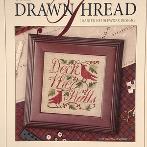 May include: A cross-stitch pattern for a holiday design featuring two red cardinals perched on a branch with holly berries and the text "Deck the Halls".
