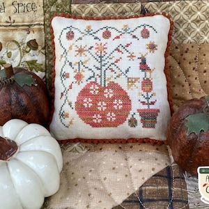 May include: A white pillow with a cross-stitch design of a pumpkin vase with flowers and a bird. The pillow is surrounded by three pumpkins, one white, one brown, and one orange. The text "Autumn Garden Palette" is visible in the lower right corner of the image.