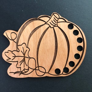 May include: Wooden yarn bowl shaped like a pumpkin with a leaf design and eight holes around the edge.