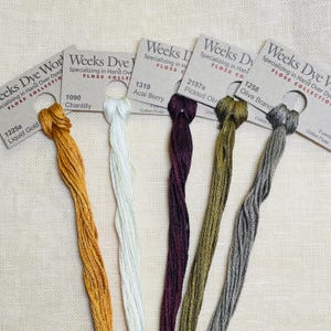 May include: Six spools of Weeks Dye Works embroidery floss in various colors, including gold, white, burgundy, olive green, and gray. Each spool is labeled with the color name and number.