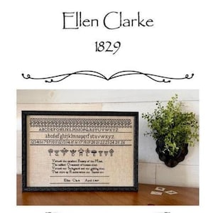 May include: A framed cross-stitch sampler with the text "Ellen Clarke 1829". The sampler features the alphabet, numbers, and a quote. The frame is black, and the background is a light tan color. A small green plant in a black wall planter is to the right.