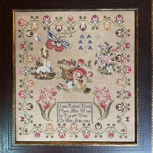May include: Framed antique cross-stitch sampler featuring a central floral arrangement, a butterfly, and a lamb. The sampler includes text that reads "Julia Rachel Dela Mare. Mer Work In The 8th Year Or Mer A.D. 1849." The frame is dark brown.