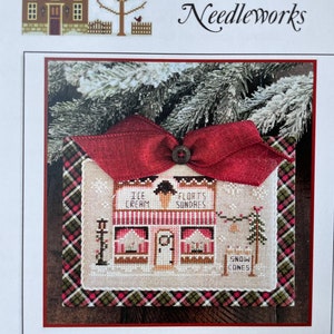 May include: Cross stitch pattern for a winter holiday scene featuring an ice cream shop with a red bow and a plaid border. The text on the pattern reads "Hometown Holiday - "Ice Cream Shop" Chart No. 24 - LHNPC - 116 - Copyright 2023".