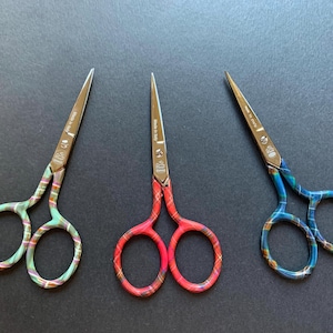 May include: Three pairs of small scissors with colorful patterned handles. The handles are patterned with red and white plaid, blue and white plaid, and green and white plaid.