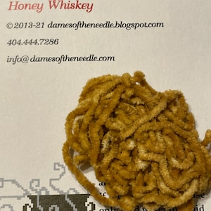 May include: A close-up of a bundle of 3 yards of Honey Whiskey chenille yarn. The yarn is a light brown color and has a fuzzy texture. The text "©2013-21 damesoftheneedle.blogspot.com" and "404.444.7286" is visible in the image. The text "info@damesoftheneedle.com" is also visible in the image.