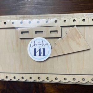 May include: A wooden craft blank with a scalloped edge frame and a small rectangular cutout. The blank is labeled "Chantelle's 141".