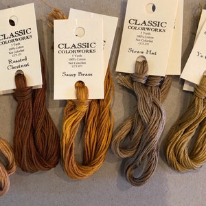 May include: Five spools of embroidery floss in various shades of brown, beige, and gold. Each spool is labeled with the brand "Classic Colorworks" and the color name: "Roasted Chestnut", "Sassy Brass", "Straw Hat", and "Ye Olde Gold".
