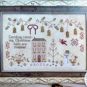 May include: Cross-stitch sampler with a Christmas theme. The design features a house, snowman, bells, and the text "Caroling, caroling, Christmas bells are ringing!" in a framed presentation.
