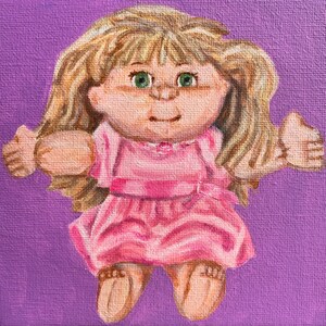 May include: A hand-painted portrait of a Cabbage Patch Kid doll with blonde hair, wearing a pink dress and smiling. The doll is painted on a purple background.