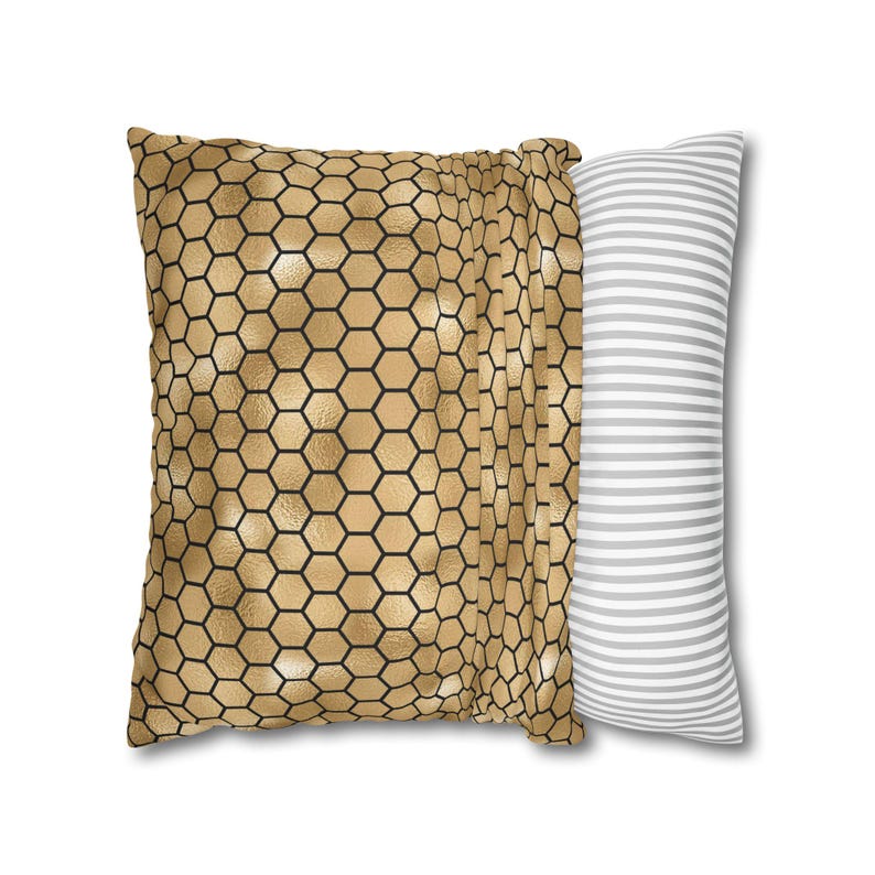 May include: A square throw pillow featuring a metallic gold honeycomb pattern with black outlines on the front and a side panel displaying a pattern of thin horizontal white and gray stripes, creating a distinct contrast between the two sides.