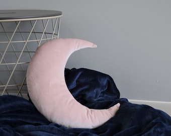 May include: A pink velvet crescent moon shaped pillow on a dark blue blanket.
