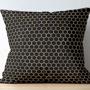 May include: A square throw pillow featuring a repeating geometric honeycomb pattern. The design consists of thin, metallic gold lines forming a grid of hexagons set against a solid, deep black background, creating a high-contrast visual effect.