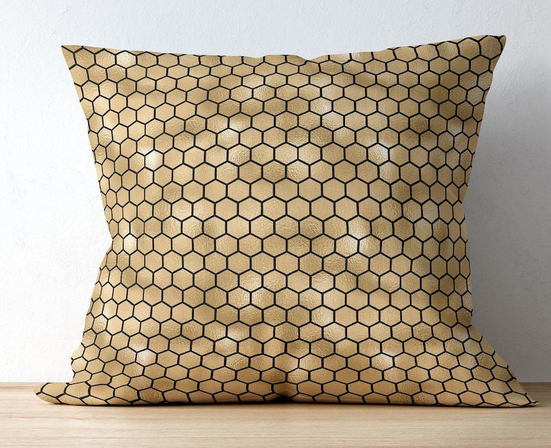 May include: A square throw pillow featuring a repeating geometric honeycomb pattern. The design consists of a metallic gold background with thin, crisp black lines forming the hexagonal grid across the entire surface of the pillow cover.