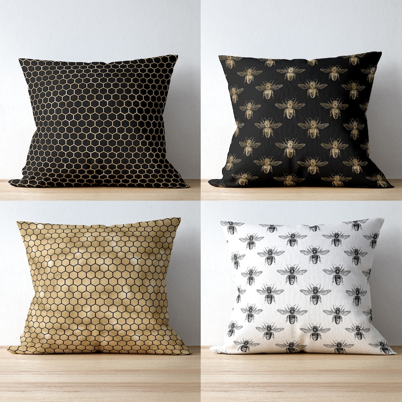 May include: A set of four square throw pillows. Two pillows feature a repeating honeycomb pattern in black and gold. One pillow has a black background with gold bee illustrations, and one pillow has a white background with black bee illustrations.