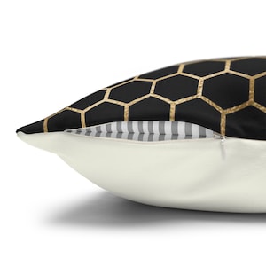 May include: A throw pillow featuring a black and gold honeycomb pattern on the top side and a solid off-white color on the bottom side. The pillow includes a visible zipper closure with a grey and white striped fabric detail along the seam.