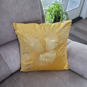 May include: A mustard yellow throw pillow with an embroidered design of white ginkgo leaves.
